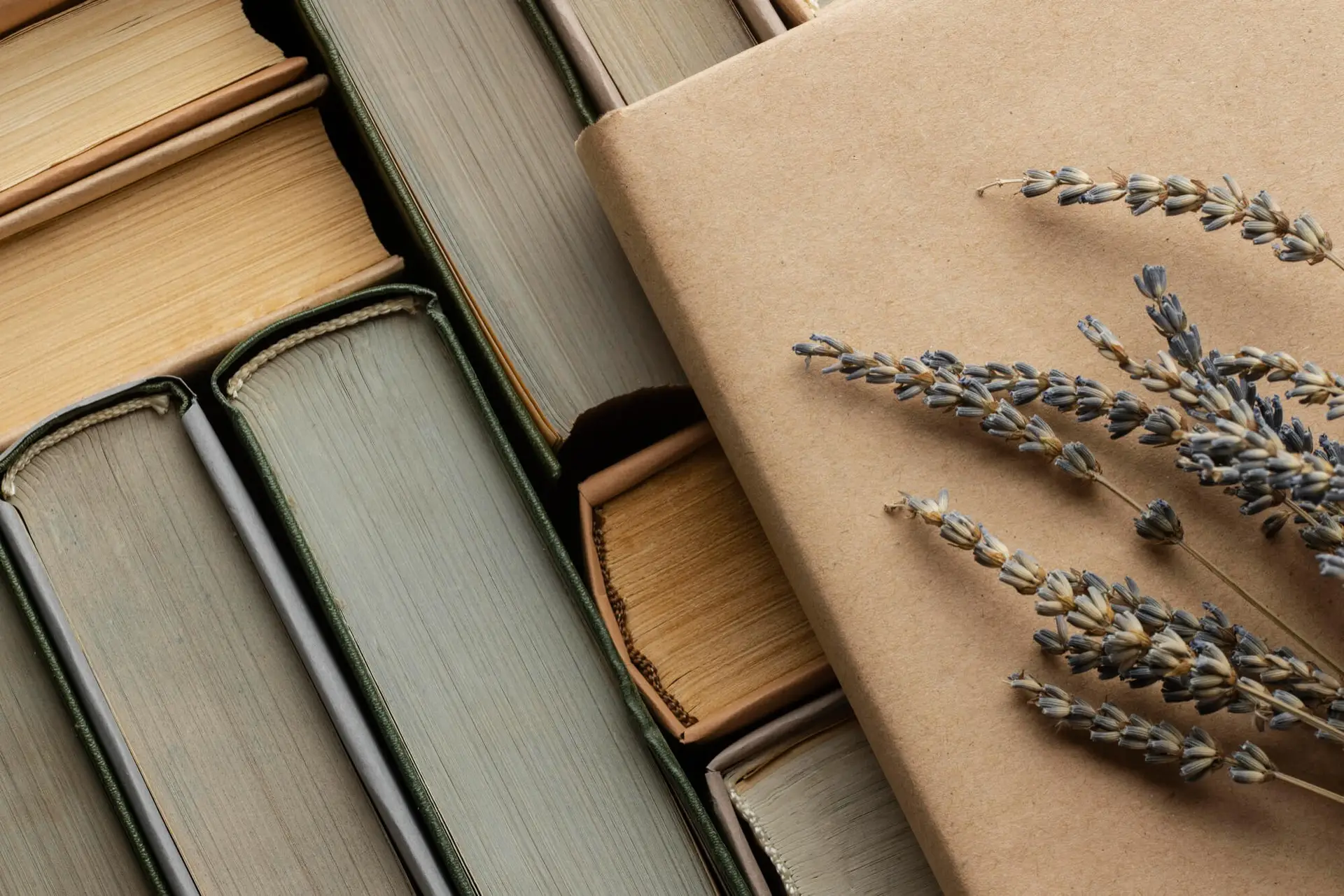 Libros en tonos beige y verde pastel amontonados de manera ordenada con un ramillete de lavanda encima.