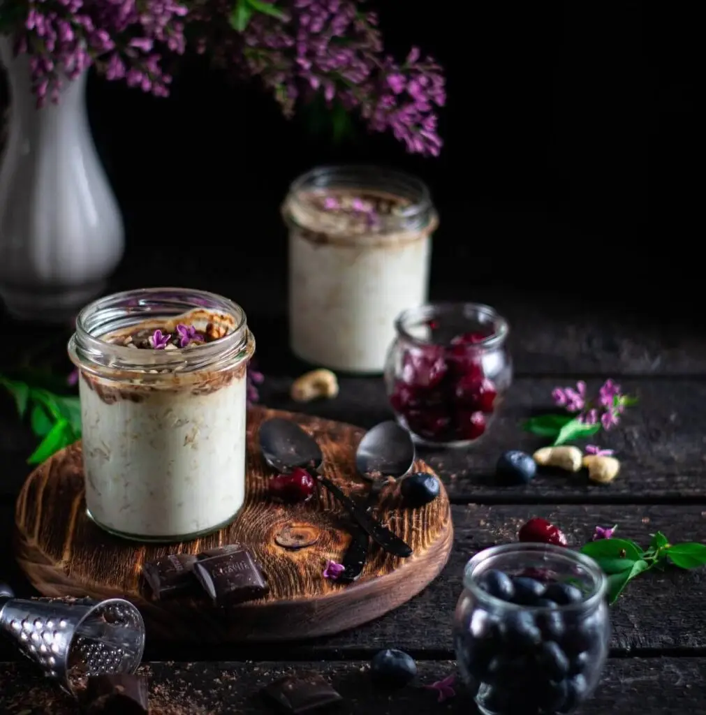 Porridge de arándanos en dos recipientes de cristal como postre. Están sobre una mesa de madera junto a un ramo de flores malvas.