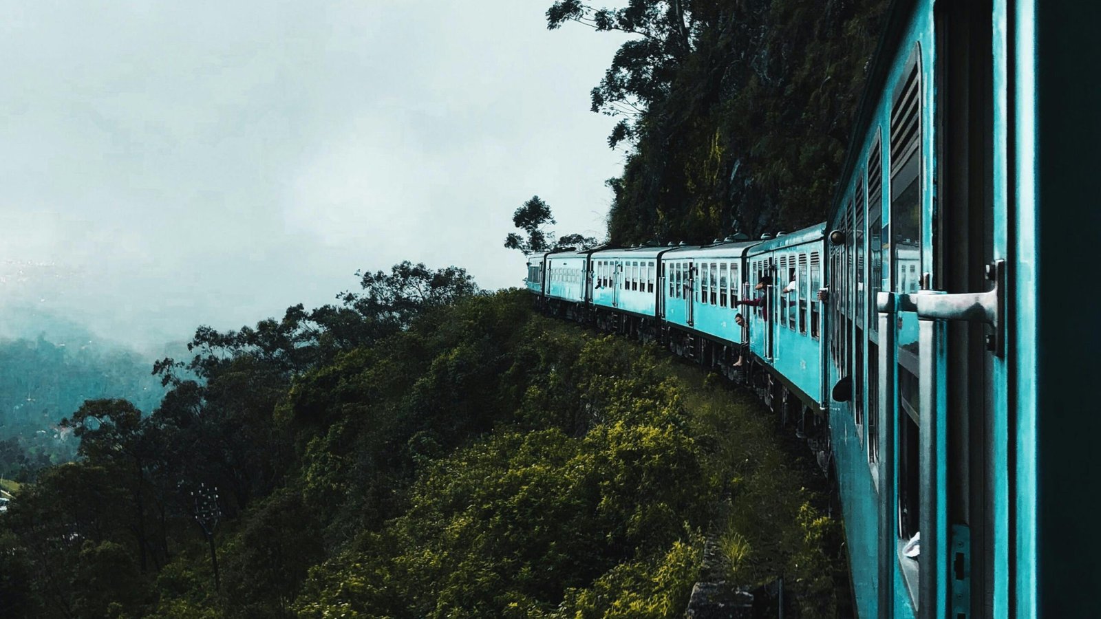 Scenic view of a blue train on a mountain curve with foggy green hills, representing the travel philosophy and the art of looking at the world from Reflejos del viaje.