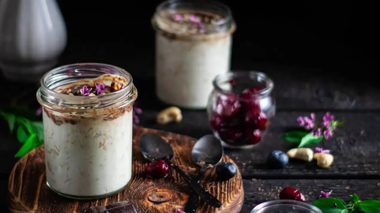 Porridge de arándanos en dos recipientes de cristal como postre. Están sobre una mesa de madera junto a un ramo de flores malvas.