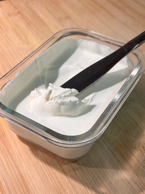 Queso crema casero en un recipiente de cristal, sobre una tabla de madera.